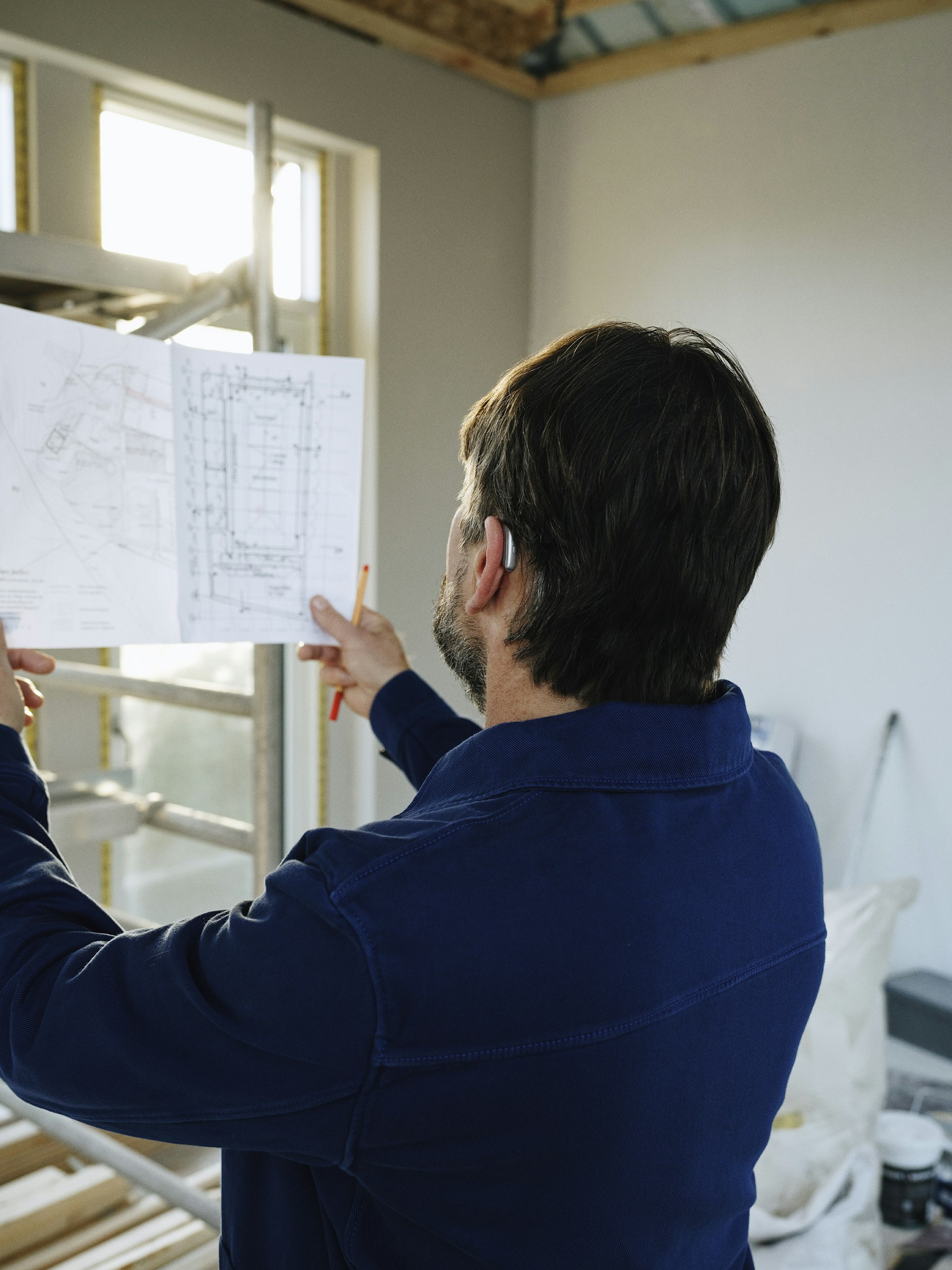 A site manager reviewing building plans against work in progress